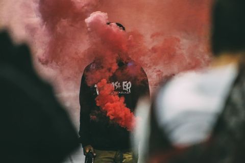 Person Surrounded by Vibrant Red Smoke in Urban Environment