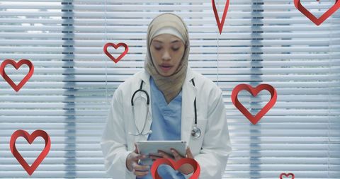 Muslim Doctor Using Tablet with Heart Symbols in Medical Office