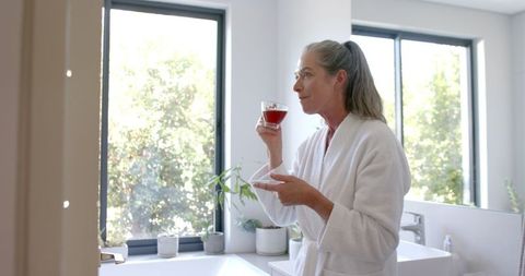 Mature woman in bathrobe relaxing with morning tea at home