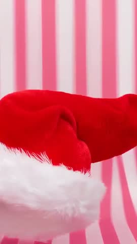 Rotating Santa Hat Swinging on Play Start Over Pink Striped Backdrop Festive Vertical Video