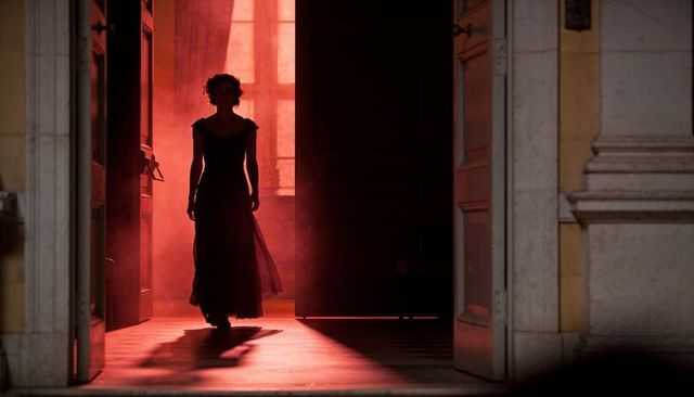 Silhouetted woman walking through grand doorway in red backlight cinematic drama with smoke