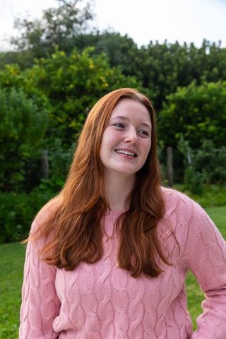 Smiling Red-Haired Woman Wearing Pink Sweater in Lush Backyard