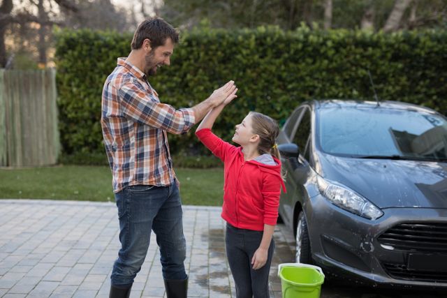  Young girl and father giving high five to each other near the car