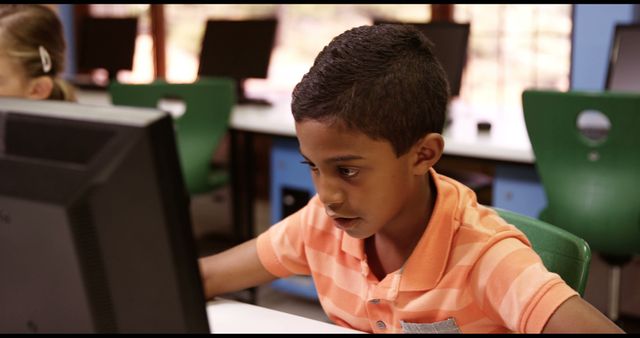Boy concentrating intently on computer screen in classroom, ideal for use in educational materials, technology in education campaigns or articles, and school marketing.
