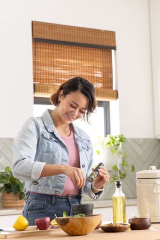 Pregnant african american woman grinding herbs in sunlit kitchen preparing salad