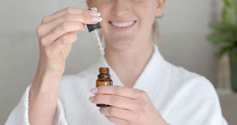 White Female in Bathrobe Using Serum Dropper for Skincare Routine