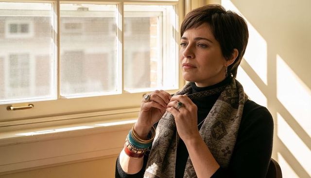 Woman adjusting scarf and bangles by sunlit window, contemplative natural light portrait