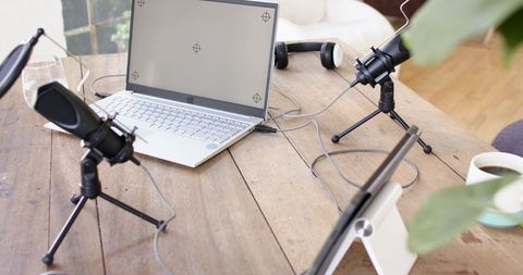 Sunlit rustic podcast recording setup with laptop, condenser microphones, headphones on wooden table