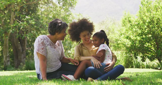 Happy biracial daughter sitting with smiling mother and grandmother outdoors in nature. Family, nature and togetherness.