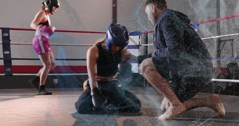 Kneeling boxer receiving coach support while resting in sparring ring