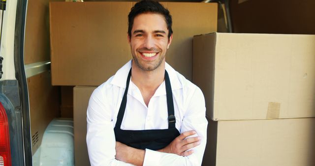 Image of smiling delivery worker with folded arms standing in a van filled with boxes. Can be used for content related to logistics, delivery services, transportation jobs, courier service marketing, and business advertisements.