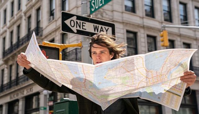 Male traveler holding large city map under one way sign wind-swept urban navigation