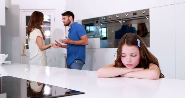 Sad young girl with head on counter while parents argue in modern kitchen. Suitable for depicting family conflict, domestic issues, emotional stress, or the impact of arguments on children in a household setting.
