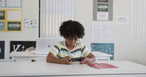 African American Boy Playing Handheld Game Focusing on Screen in Classroom