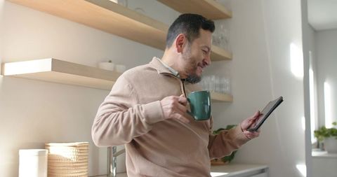 Relaxed Asian Man Enjoying Tablet Coffee Break in Modern Kitchen