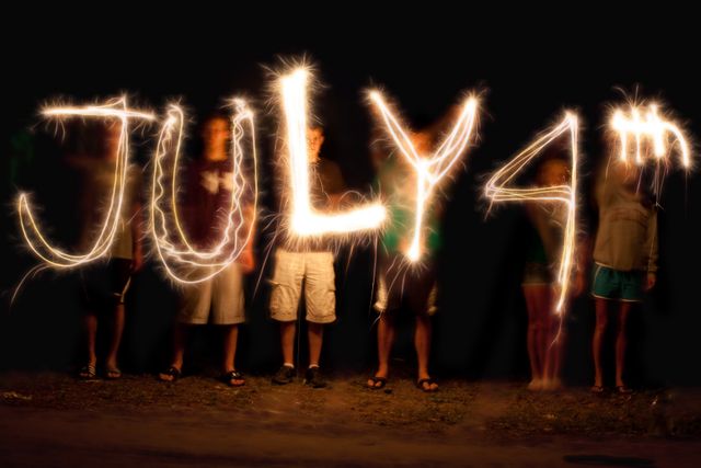 People write 'July 4th' with sparklers during a nighttime celebration of USA Independence Day. The image uses long exposure to capture the glowing light trails, creating a festive and dynamic display. Ideal for promoting July 4th events, patriotic celebrations, holiday-themed marketing, and festive greetings.