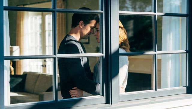 Sunlit couple embracing at window showing engagement ring and quiet intimacy