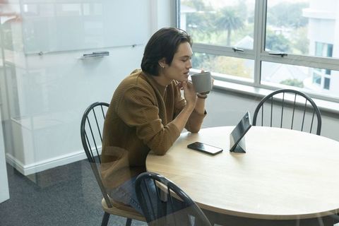 Young Asian man sipping coffee while viewing tablet at modern office round table