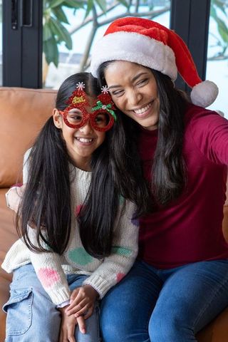 Mother and daughter taking festive selfie wearing santa hat and holiday glasses