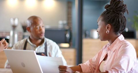 Coffeehouse collaboration reviewing documents at laptop with barista during casual meeting