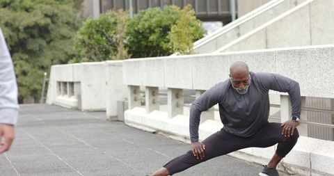 Mature african american man performing deep side lunge on urban plaza wearing smartwatch