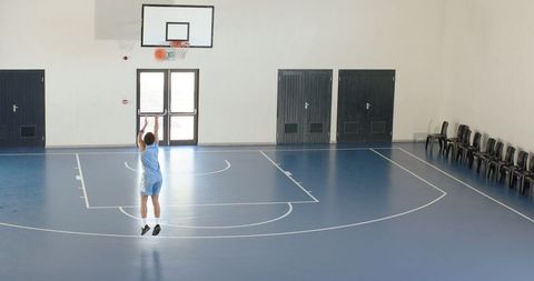 Man Practicing Basketball Indoors on Blue Court