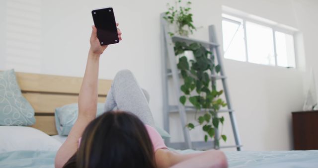 Young woman lying on bed using smartphone for selfie in bright bedroom - Download Free Stock Images Pikwizard.com