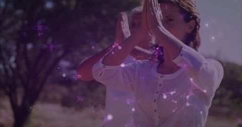 Couple practicing outdoor meditation pressing palms together with purple light overlay