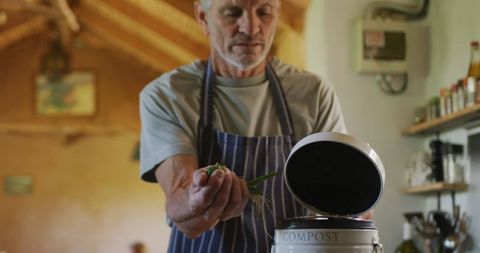 Senior Caucasian Man Composting Vegetable Cuttings in Kitchen