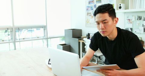 Focused asian business executive working with laptop and tablet in modern office