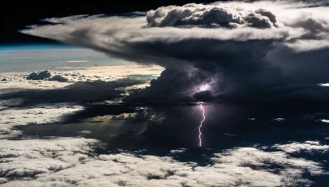 Anvil thunderhead releasing luminous lightning over layered cloud deck and shadowed sky