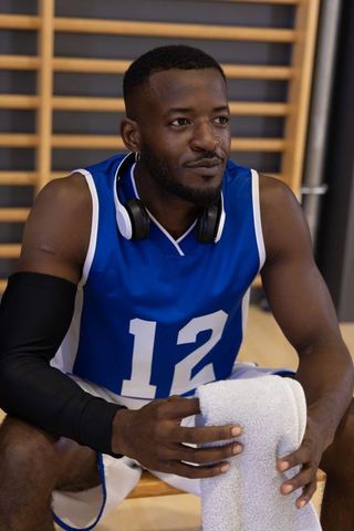 Preparing for game: basketball athlete sitting on bench holding towel and headphones