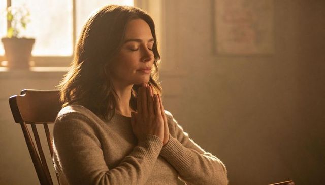 Woman meditating with hands together in sunlit room, peaceful mindfulness practice