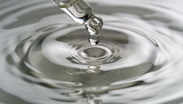 Clear pipette releasing droplet creating concentric monochrome ripples on water surface