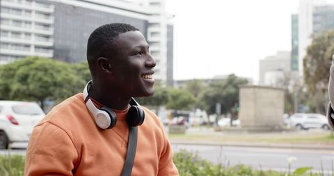 African American Man Smiling on Urban Bench Wearing Headphones and Orange Sweatshirt