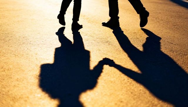 Couple holding hands casting long shadows on sunlit pavement during golden hour silhouette