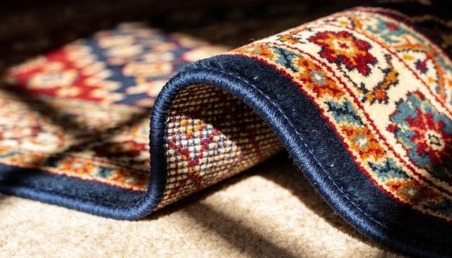 Handwoven oriental rug edge lifting on carpet revealing intricate knots and navy binding