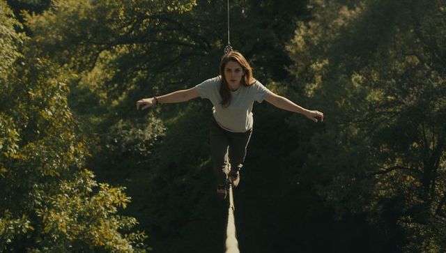 Woman striding boldly on slackline amid forest canopy