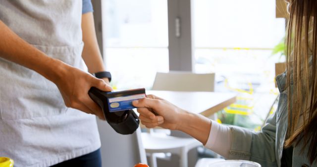 A young Caucasian woman is making a contactless payment using a credit card to a waiter, with copy space. Contactless payments have become increasingly popular for their convenience and hygiene benefits.