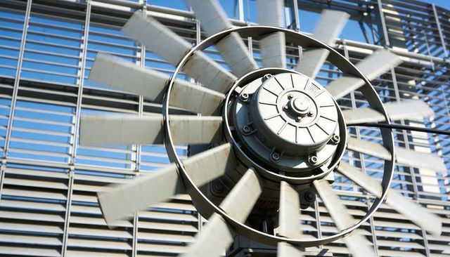 Spinning industrial axial fan with blurred blades on louvered rooftop facade, metal hub