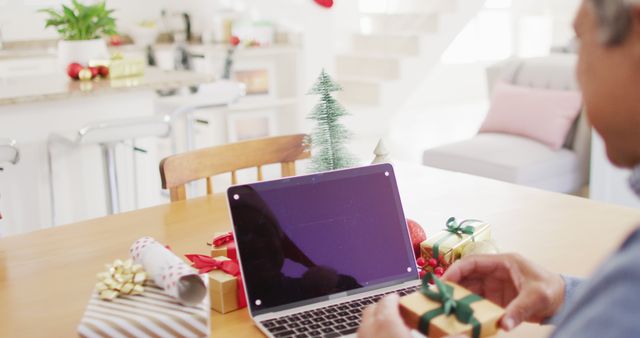 Image of senior biracial man holding gift making laptop christmas image call, copy space on screen. Christmas, tradition, global communication, inclusivity and senior lifestyle concept.