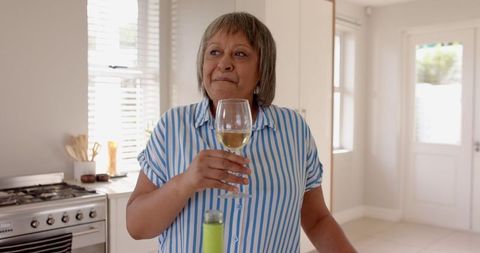 Senior Woman Enjoying White Wine In Modern Kitchen