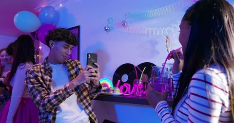 Neon House Party with Diverse Young Adults Mingling, Man Framing Smartphone Selfie