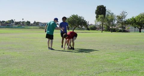 Coach gesturing while guiding players placing marker on grassy field during training