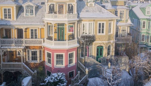 Snow-dusted pastel victorian rowhouses showcasing bay windows, porches, ornate trim