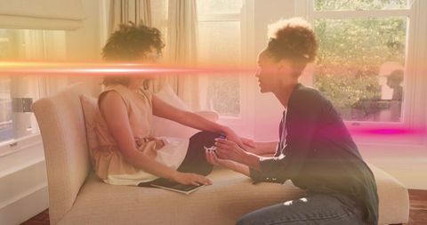 Applying manicure for friend on sunlit living room chaise, intimate at-home beauty moment