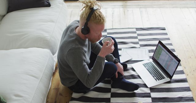 Albino african american man with dreadlocks siting on the floor, working and using laptop. remote working using technology at home.