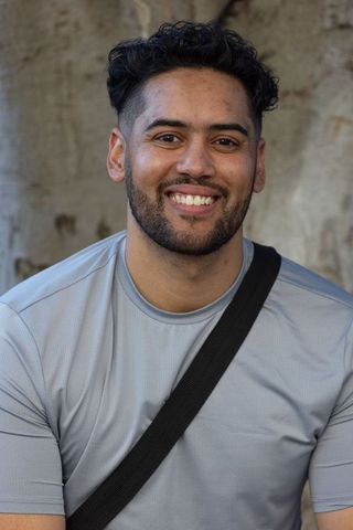 Smiling young man in light-gray athletic shirt with black crossbody strap outdoor portrait