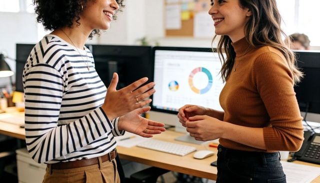 Women collaborating at office workstation discussing data with colorful donut chart