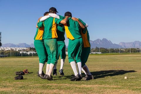 Cricket team huddling on grassy field celebrating teamwork and unity in green kit